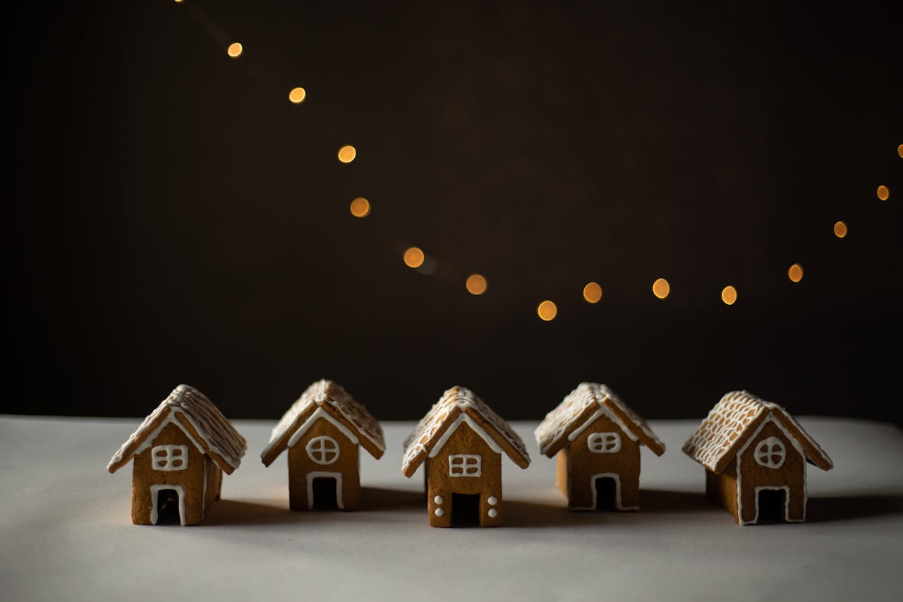 Five gingerbread houses with icing details, set against soft golden bokeh lights creating a cozy holiday feel.
